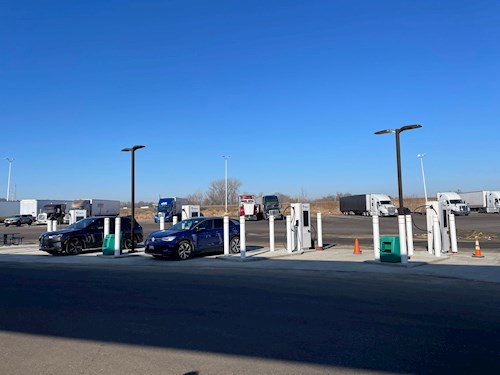 four electric vehicle chargers with two cars using them