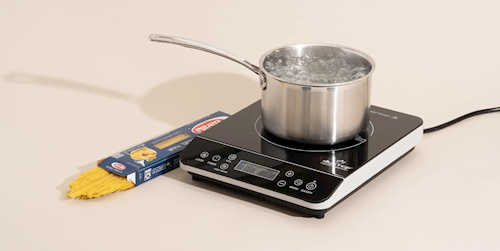 Uncooked pasta sits next to water boiling on a portable induction cooktop.