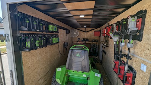 Green electric lawn mower charging inside custom work trailer