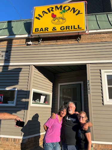 Three people posing in front of Harmony Bar & Grill